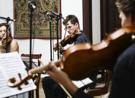 A photograph. A string concert in Villa Decius. The musicians play the violin and the cello in the Ball Room at Villa Decius.